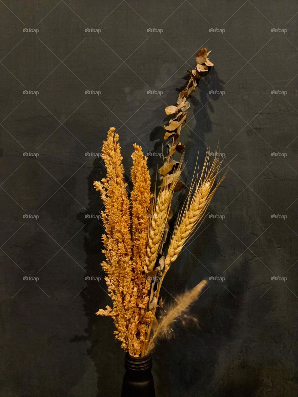 Dried flower
bouquet in black
glass bottle on
wooden table
against dull black
wall background.
Place for text or
advertisement.
View from above