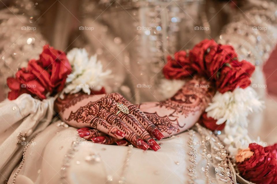 a bride's hands adorned with intricate henna designs, vibrant red and white flower bangles, and a delicate gold ring.
