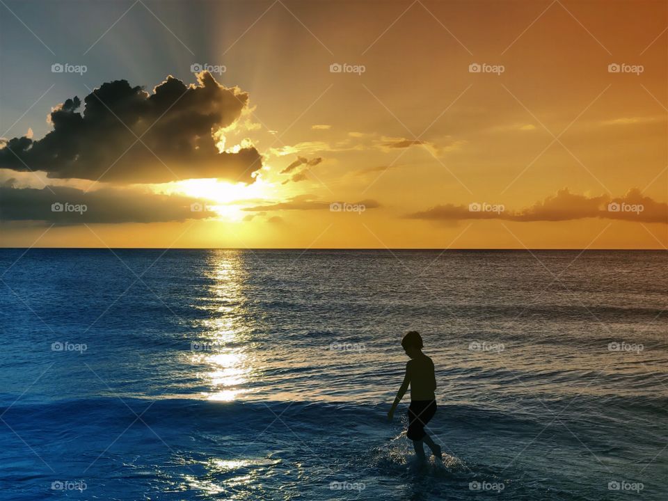 Small boy playing in the ocean in the light of a dazzling sunset.