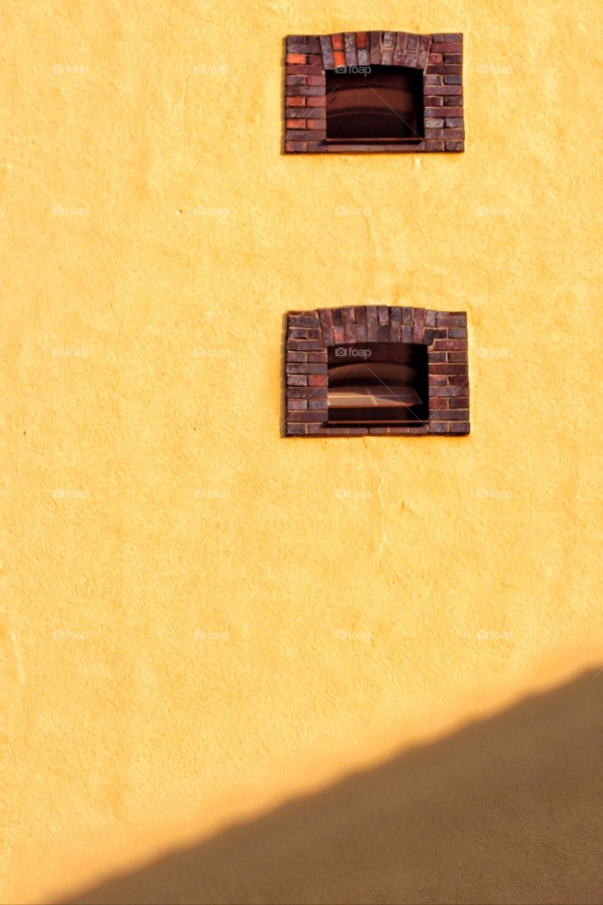 Yellow house wall in sunlight with two brick windows