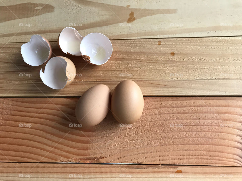 two fresh chicken eggs with four pieces of eggshells on natural rubber wood board with copy space on right side of frame