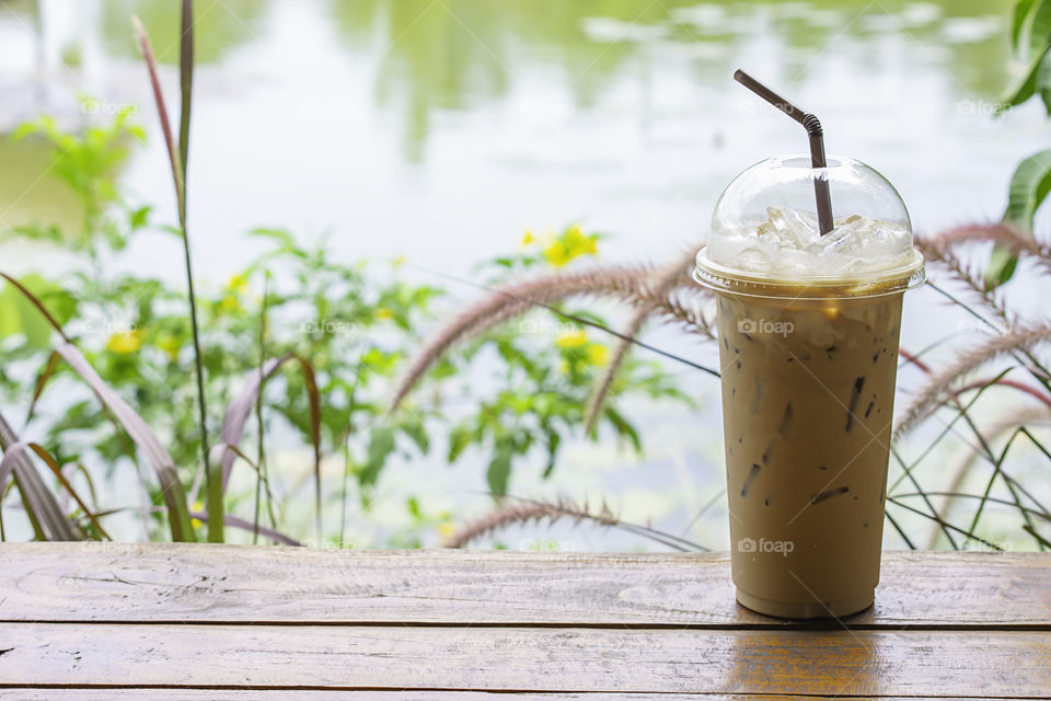 Iced coffee in glass on the table Background  Pennisetum pedicellatum and pond.