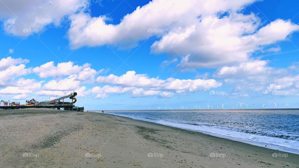 Dramatic blue sky and clouds over sandy beach and ocean. Pier and wind turbines can be seen too. Taken on Great Yarmouth beach.