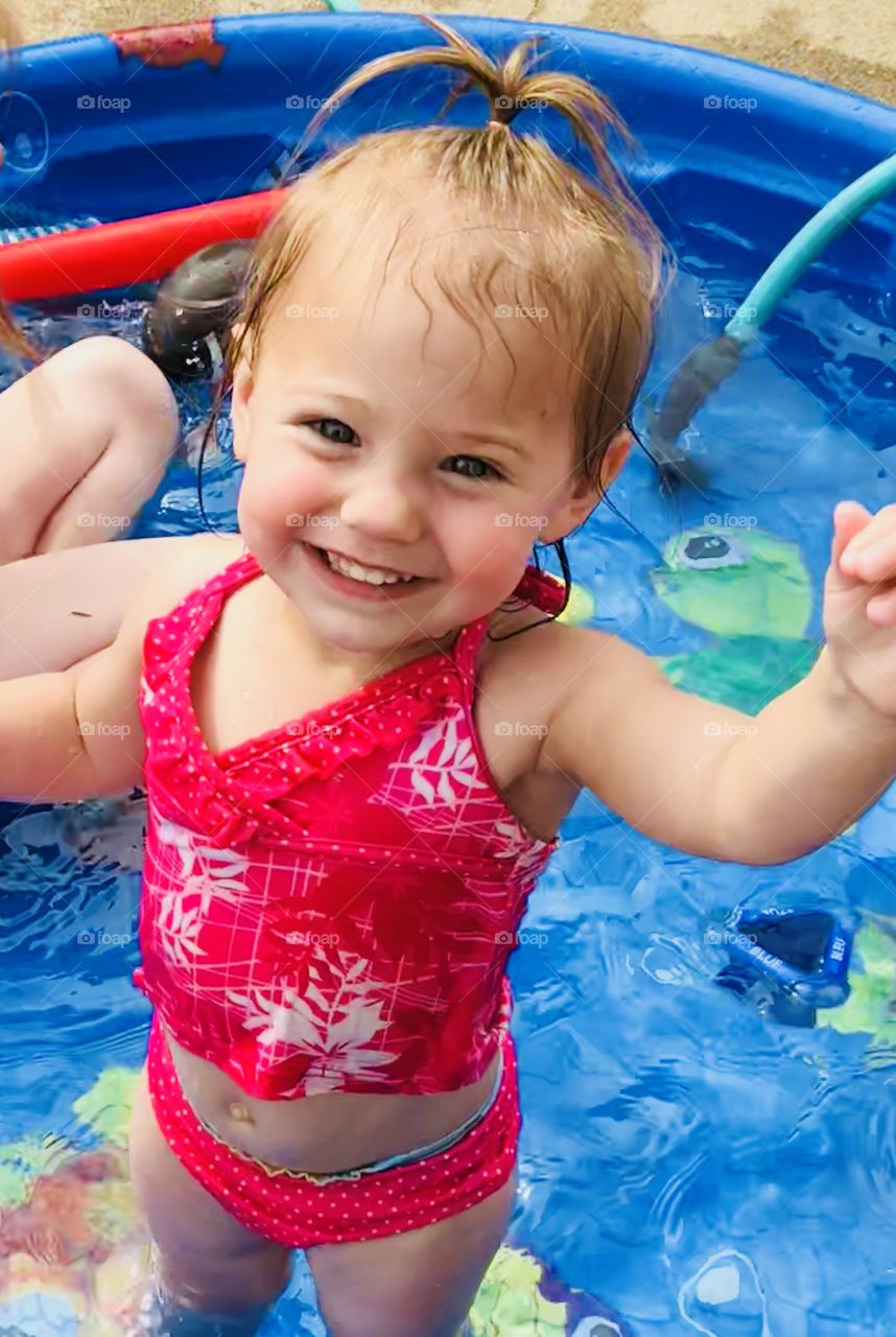 Toddler girl in swim suit playing in small pool