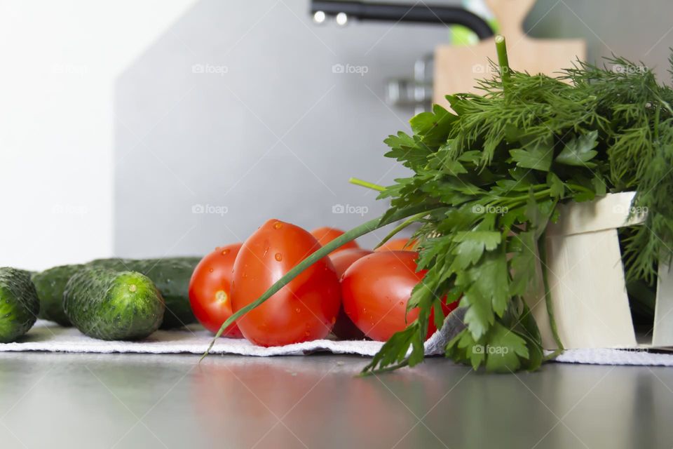 Fresh, bright, juicy vegetables and herbs for preparing salads and other vegetable dishes are on a gray, kitchen worktop.
