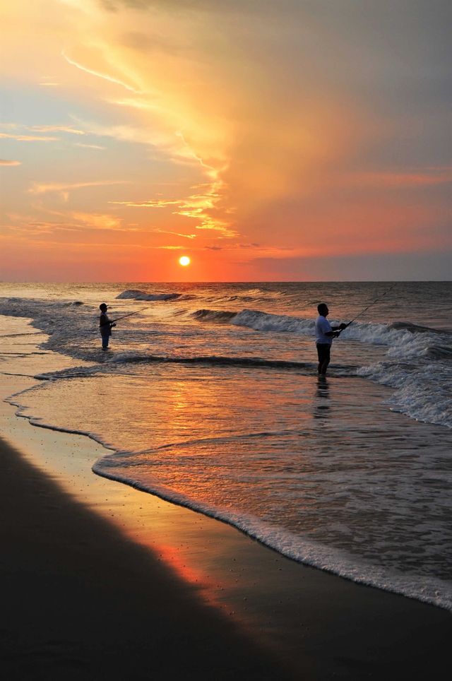 Silhouette of a young boy and his Father surf fishing at Sunrise In Myrtle Beach South Carolina. 