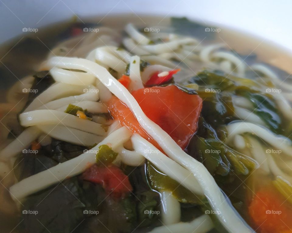 Close-up of a broth-based soup with noodles, tomato and spinach.