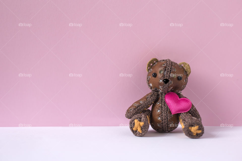 Toy bear with pink heart is sitting on the pink background