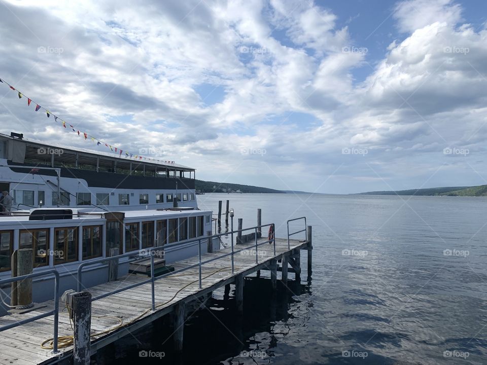 A dock on a calming lake with some beautiful clouds and a fantastic sky. The water has a nice reflection and looks phenomenal. Amazing photo with good lighting, and positioning. 