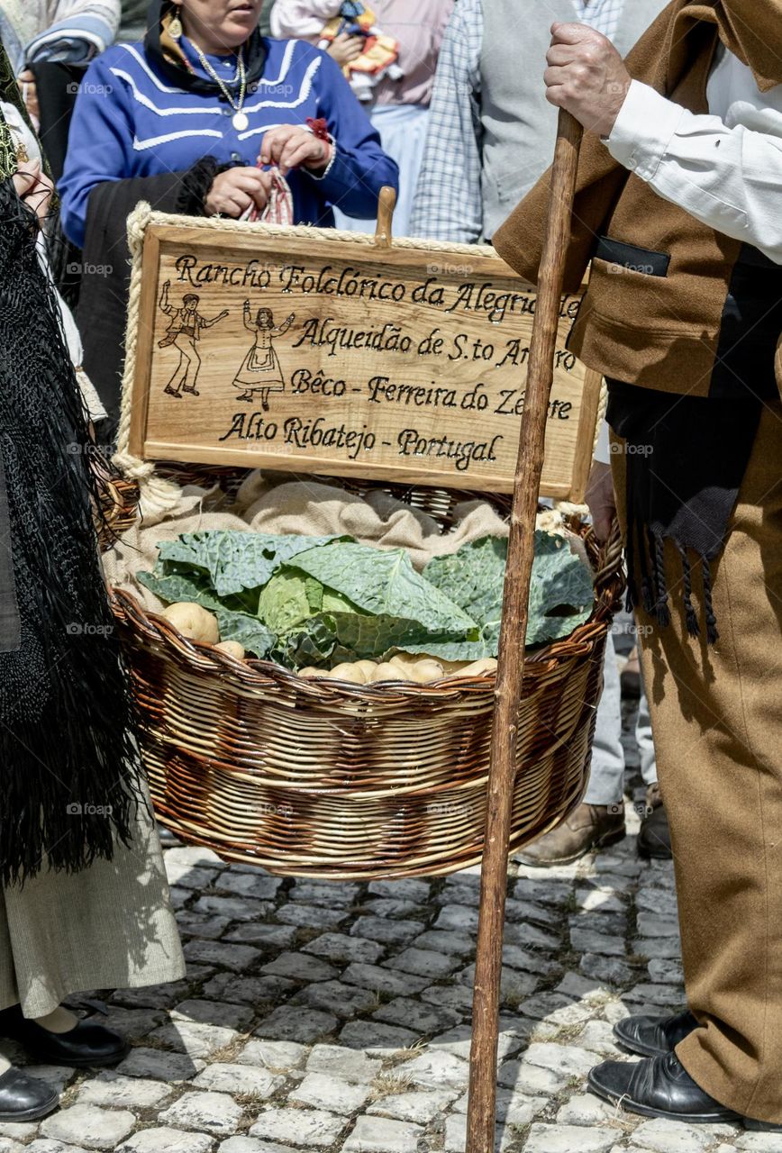 People dressed up in traditional costume, carrying a basket of fresh produce as part of a local festa.