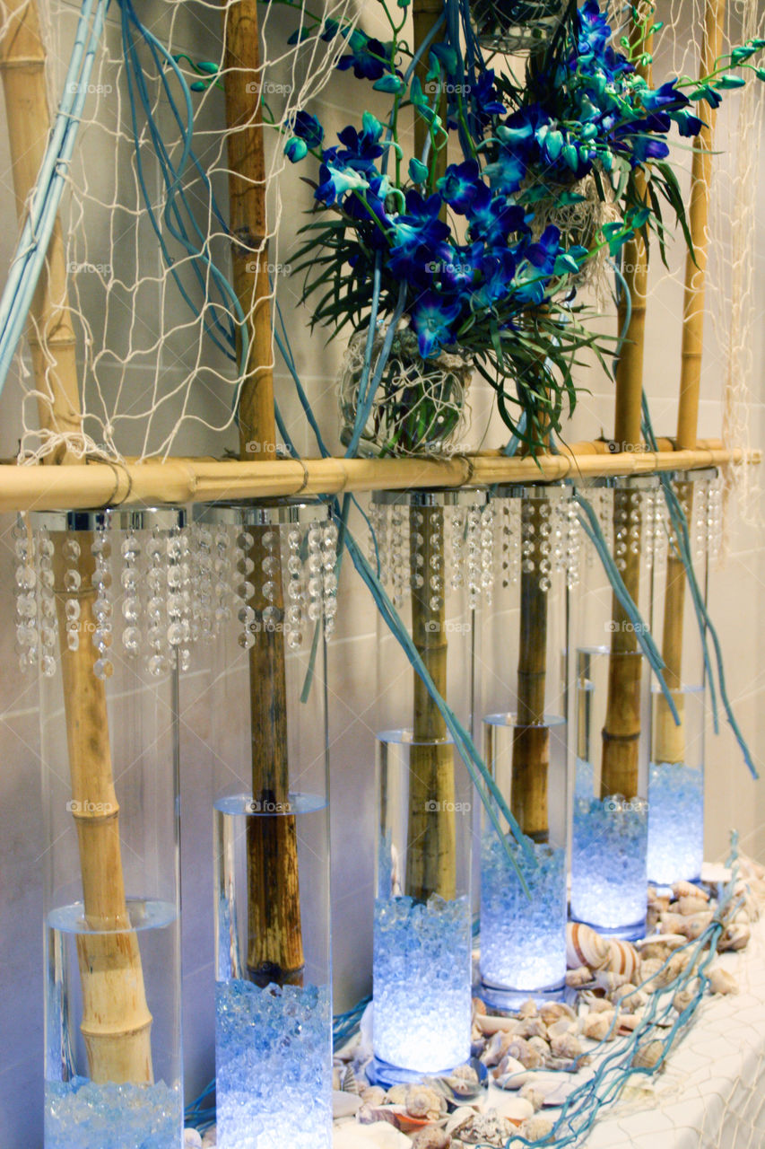 Bamboo stalks in illuminated vases adorned with decorative crystals and seashells at an event