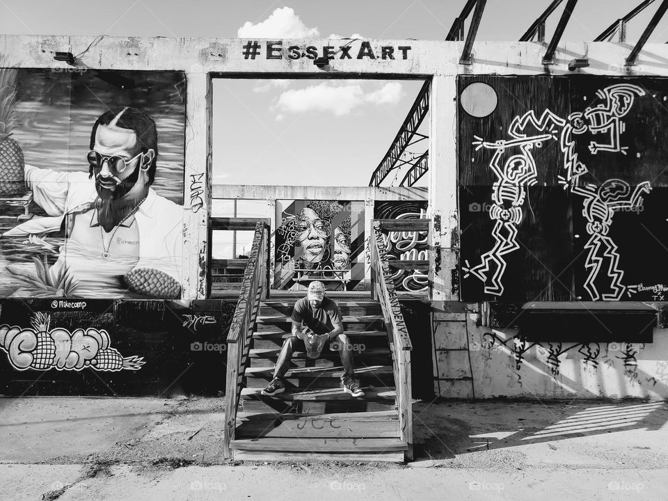 Black and white:  Man sitting on stairs surrounded by Urban outdoor art.