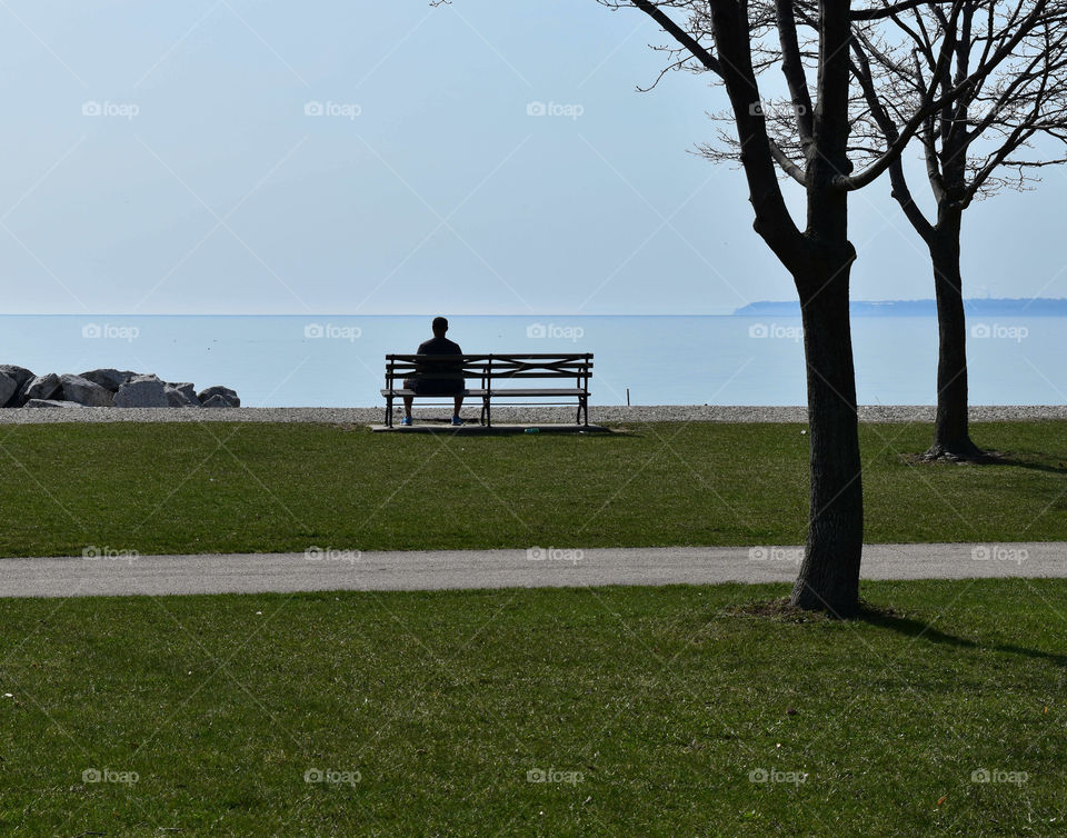 Sillouette of a man sitting on a bench staring at the Lake shore