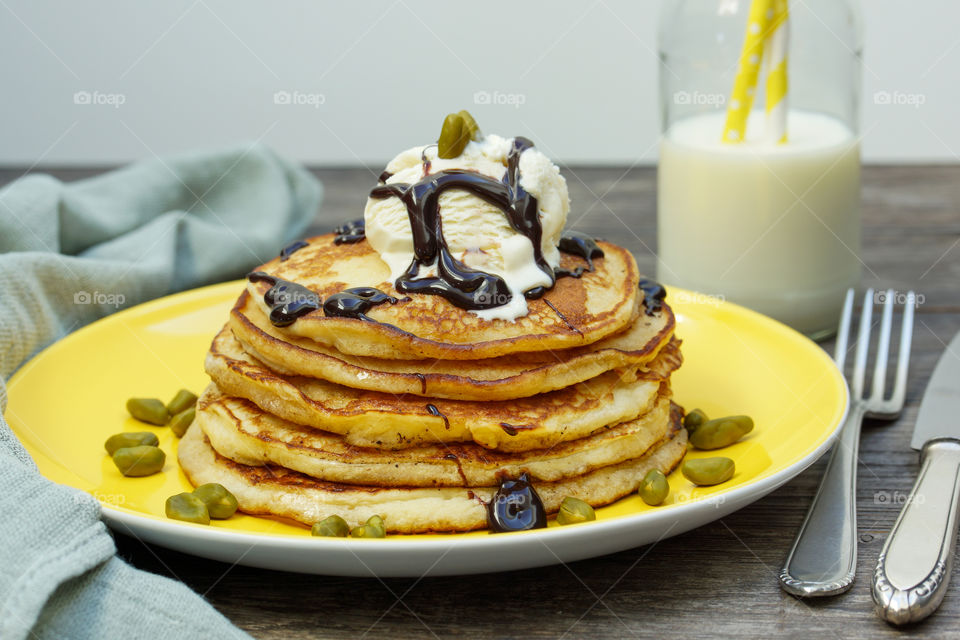 stack of pancakes with icecream, chocolate sauce and pistachios