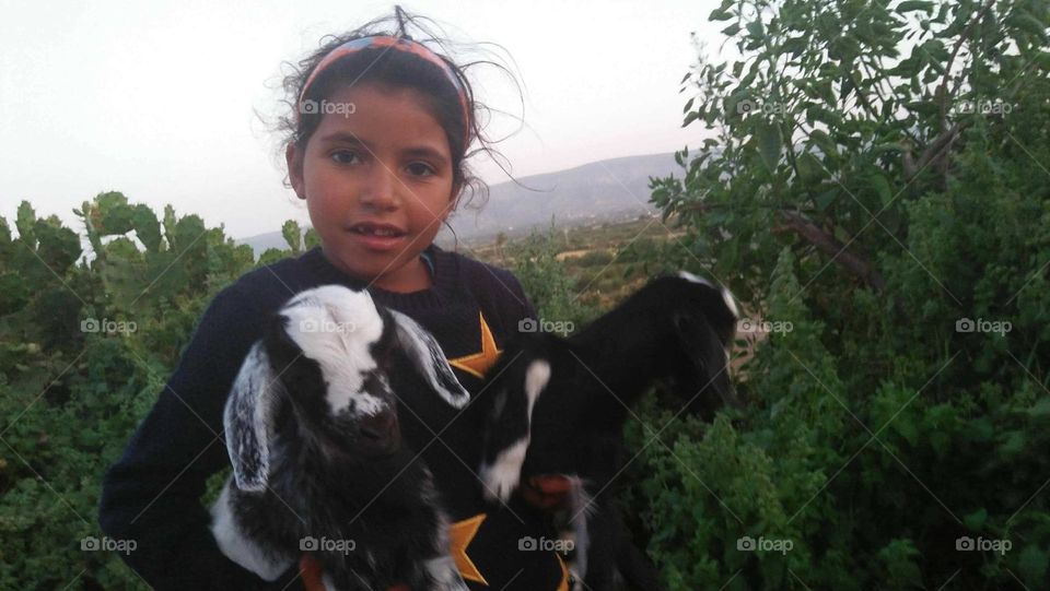 A beautiful girl holding two small black goats