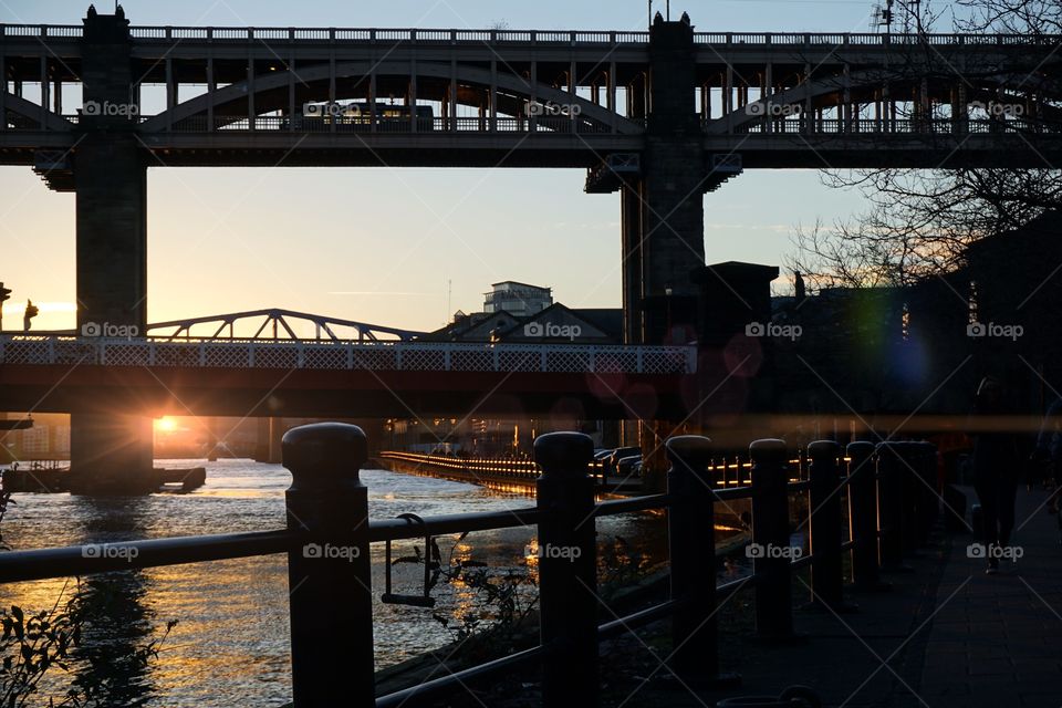 Golden river water lit up by the setting sun amongst Newcastle-Upon-Tyne’s many bridges ...