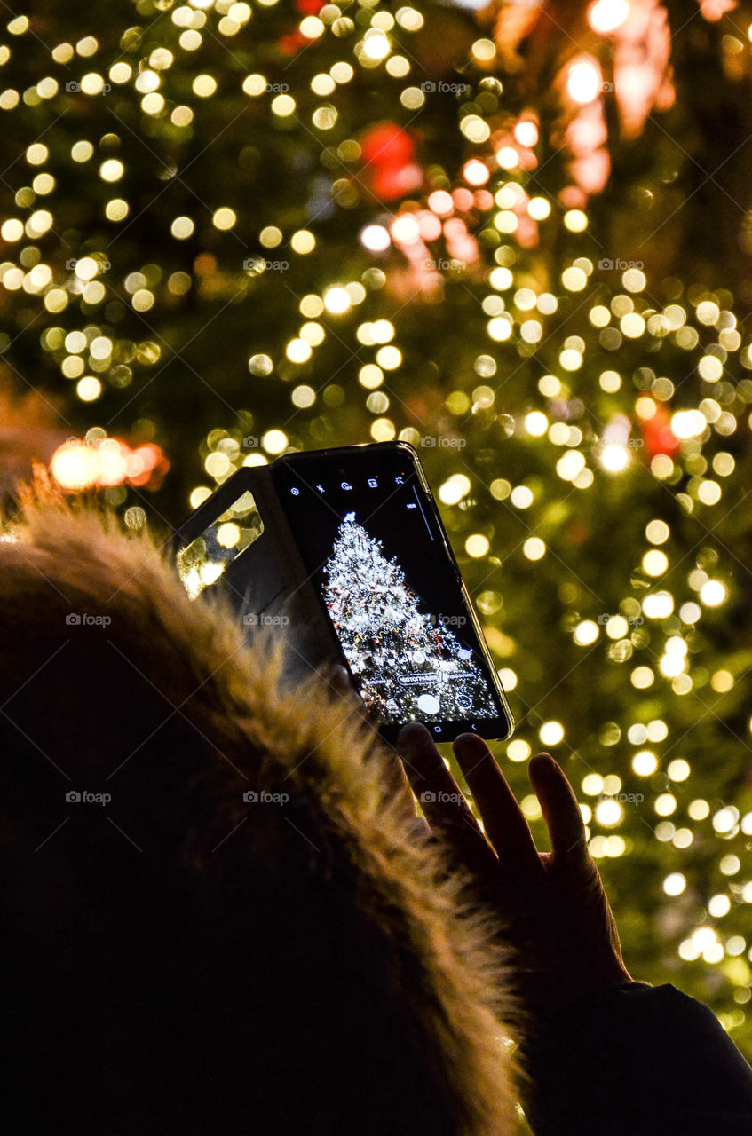 Person takes a picture of the new year tree on smartphone.