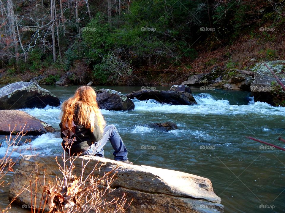 girl setting on large boulder, admiring the Chauga river in South Carolina