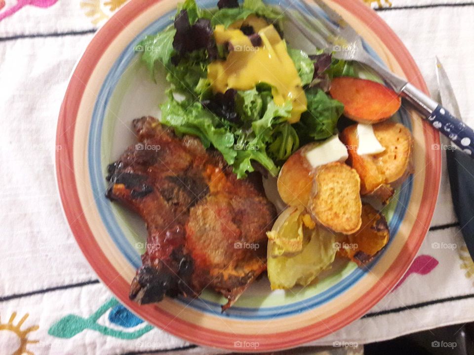 chuletas asadas, batatas y papa's asadas y ensalada Verde. (grilled pork chops, baked sweet and regular potatoes and green lettuce salad)