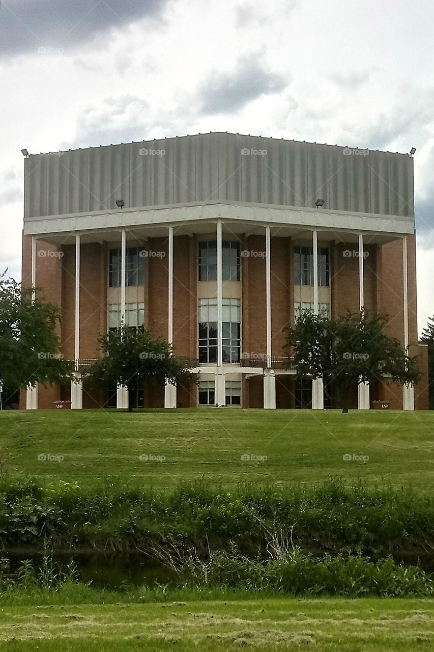 a large brick auditorium with a field of grass in front of it