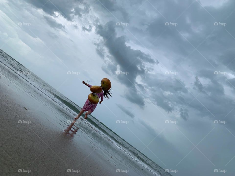 Little Girl Jumping And Running Having Fun With Helium Emoji’s Balloons On The Beach By The Ocean.