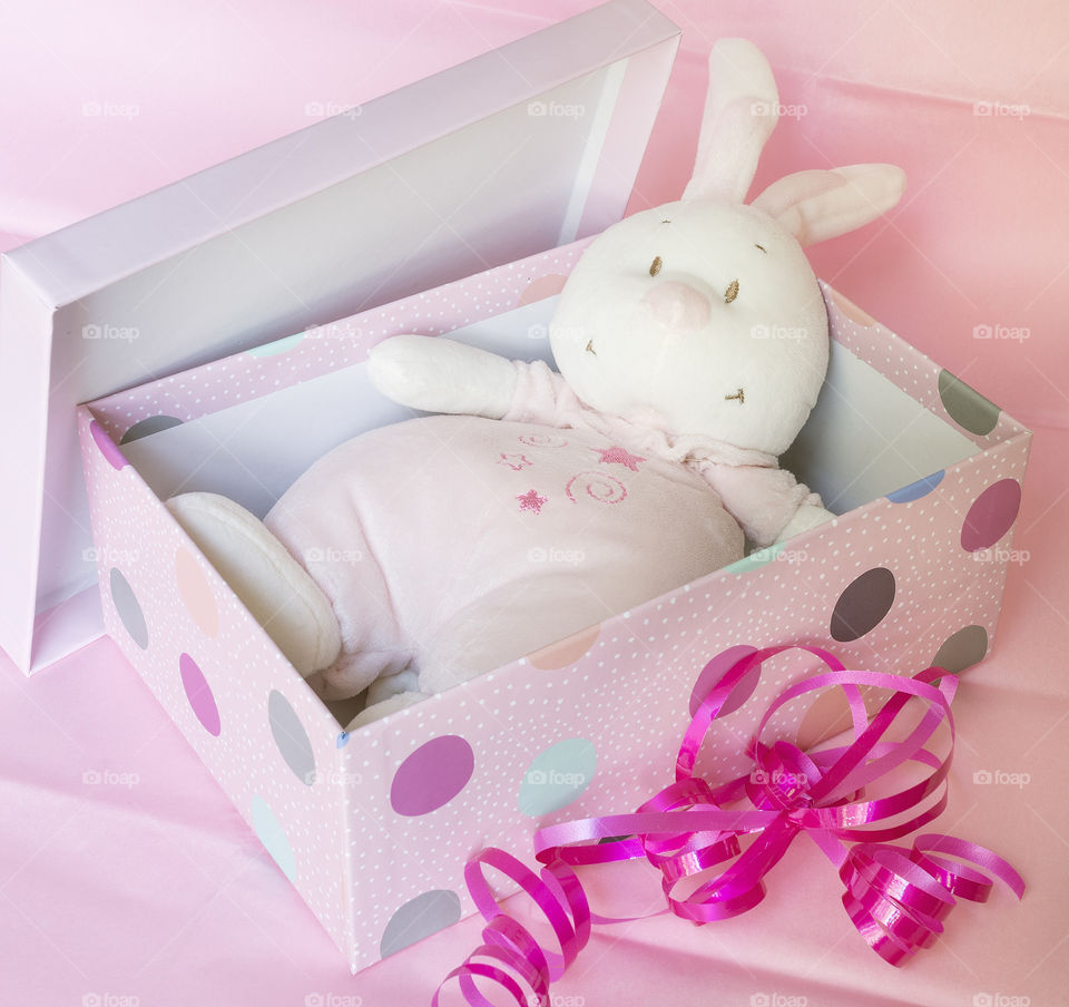 A soft pink toy rabbit in an open spotted pink gift box with pink ribbon.