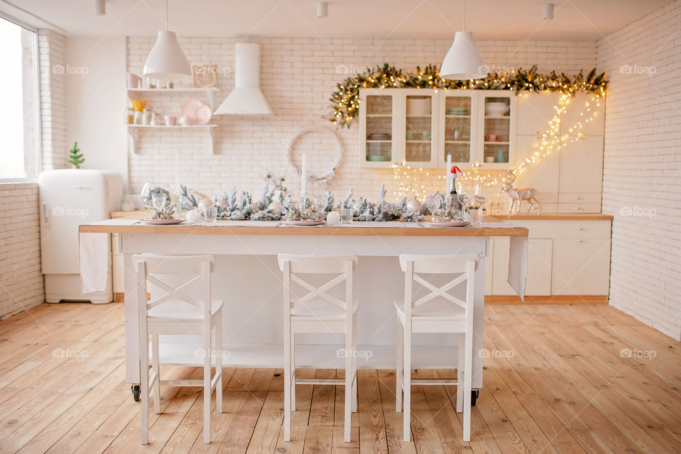 Festive winter cozy kitchen interior with garlands, decorations and gifts.  Christmas dinner at the decorated table.