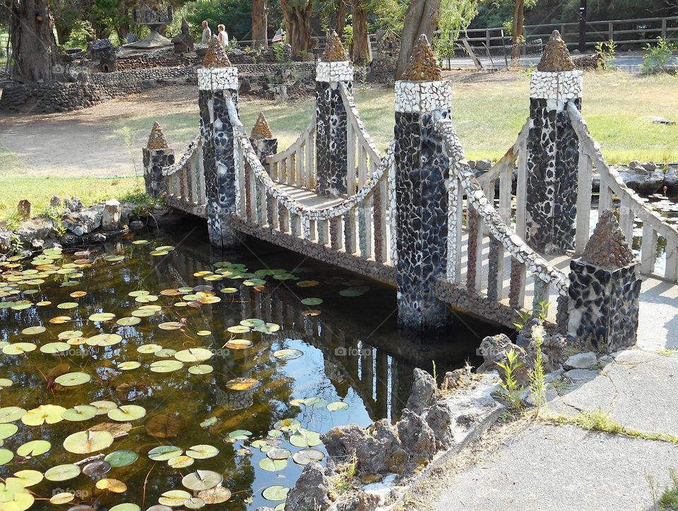 A beautiful and ornate rock bridge on a peaceful path crosses a fairytale style mote with lots of Lillie Pads at Peterson’s Rock Garden on a sunny summer day in Central Oregon.