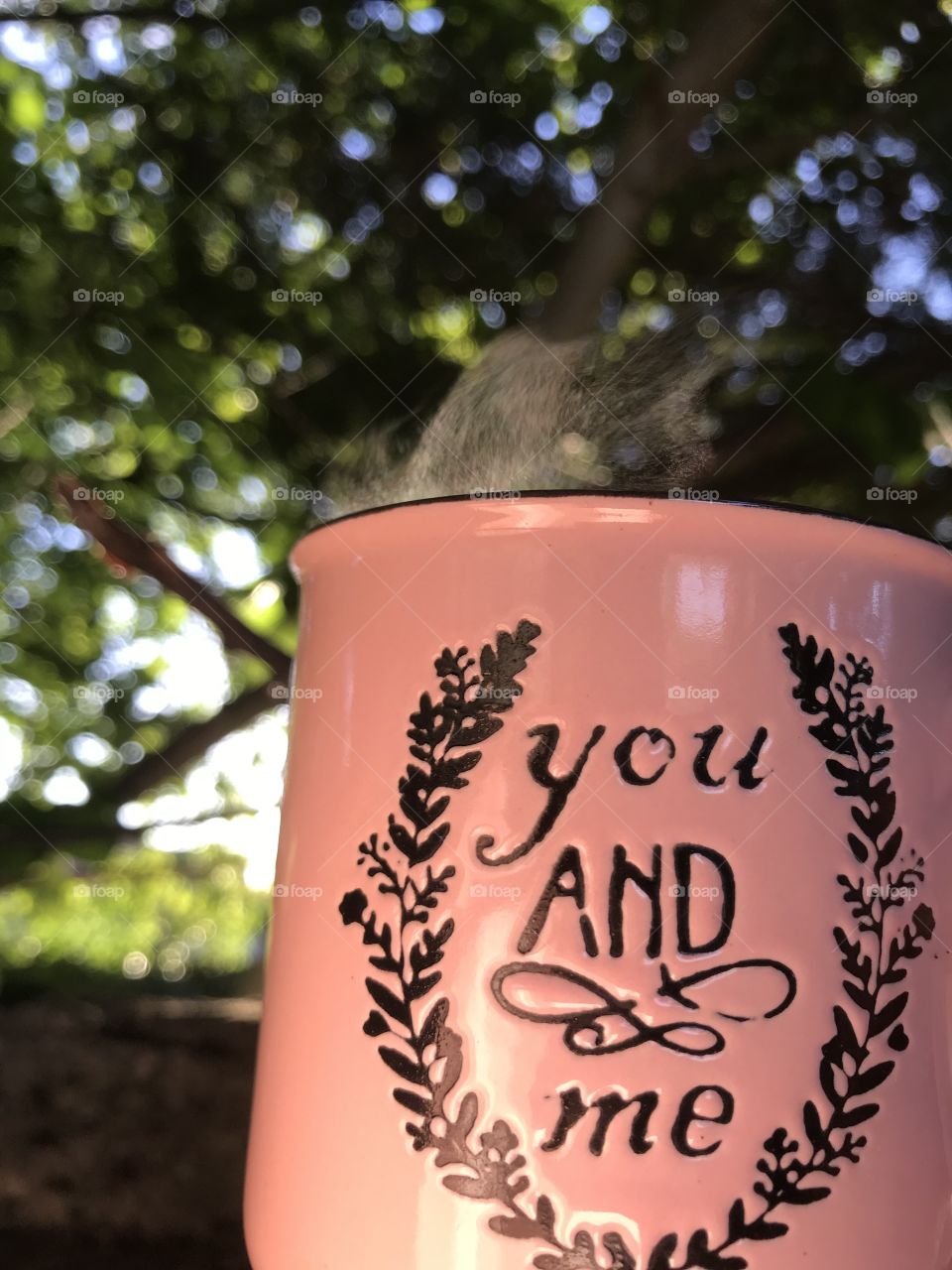 Lovely pink porcelain cup of coffee with black coffee in it, in the beautiful morning, surrounded by green trees.