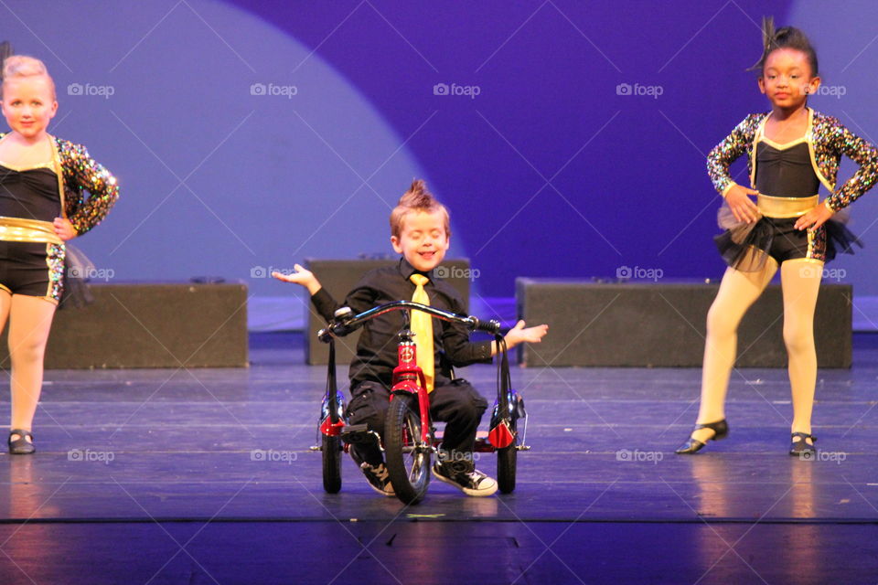 What? I know I'm cute. Boy riding tricycle in dance recital