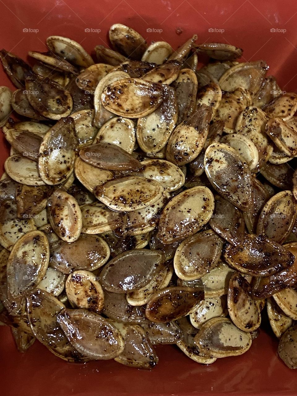 Roasted pumpkin seeds in a red bowl.