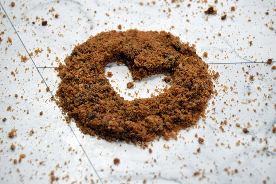 A small heart hollowed out of the centre of a sprinkling of chocolate chip cookie crumbs on a white marble flatlay background.