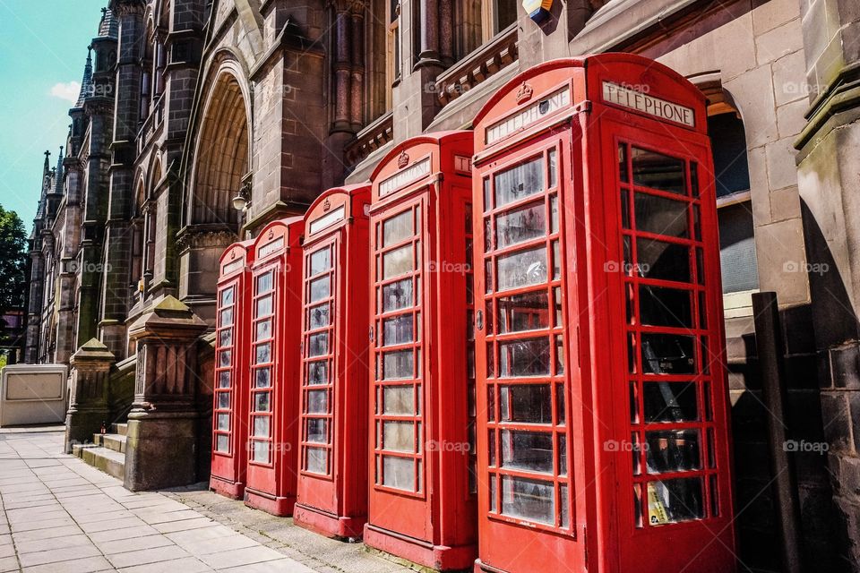 Row of traditional red British telephone boxes outside Victorian building with no people. 