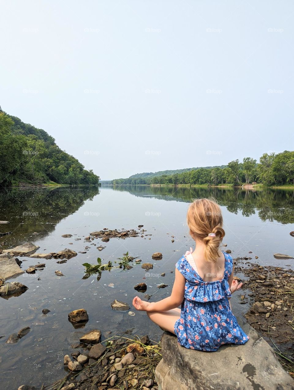 girl sitting on a rock meditating, enjoying stillness watching the calm river water