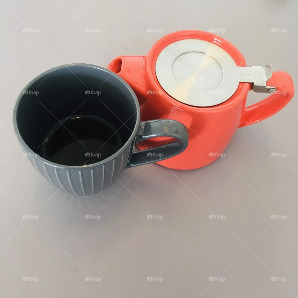 Cup and teapot nestled together on a smooth grey background