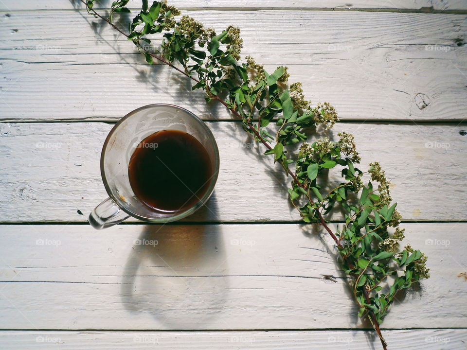 A cup of black coffee and a dry branch with flowers on white boards