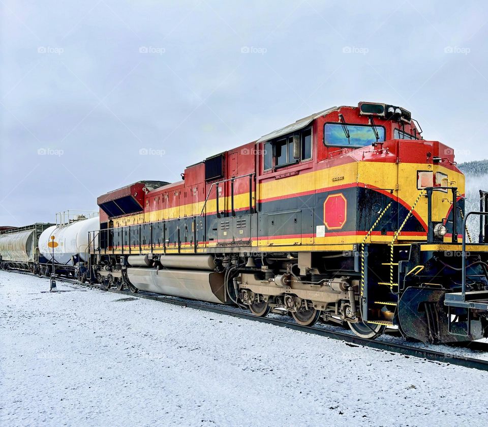A brightly coloured train engine against the snow covered ground.