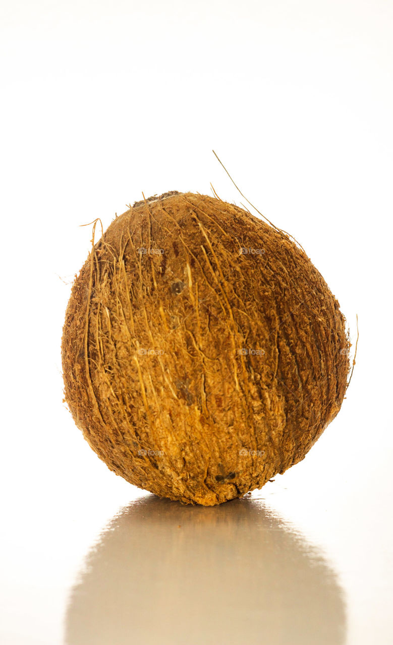 Coco seco, descascado sobre uma superfície branca e com o fundo branco.