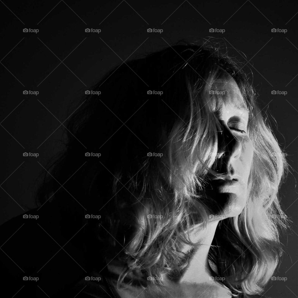 Woman with closed eyed and blond curly hair low key black and white portrait