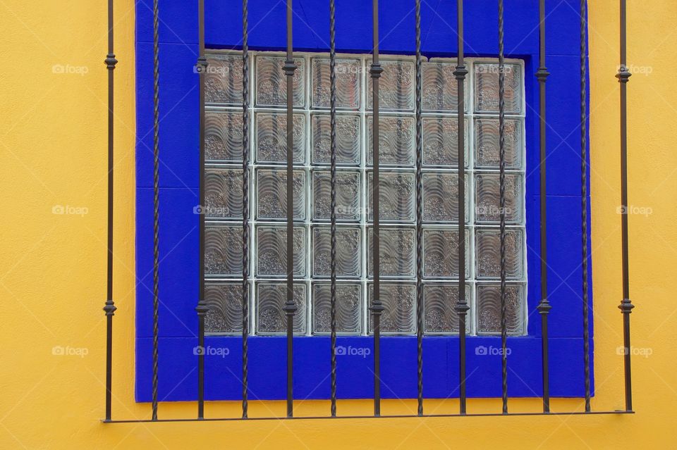 A colorful image of an exterior window made up of 36 square glass blocks and a wooden purple frame in San Miguel de Allende, Mexico.