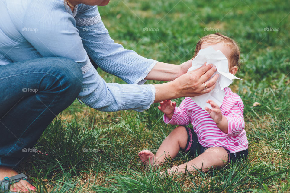 Mom wiping nose her little daughter with a tissue