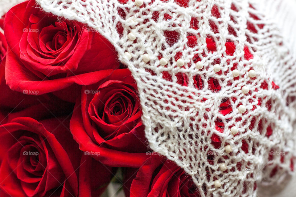 A hand knit and beaded wedding shawl rests on a perfect bouquet of red roses