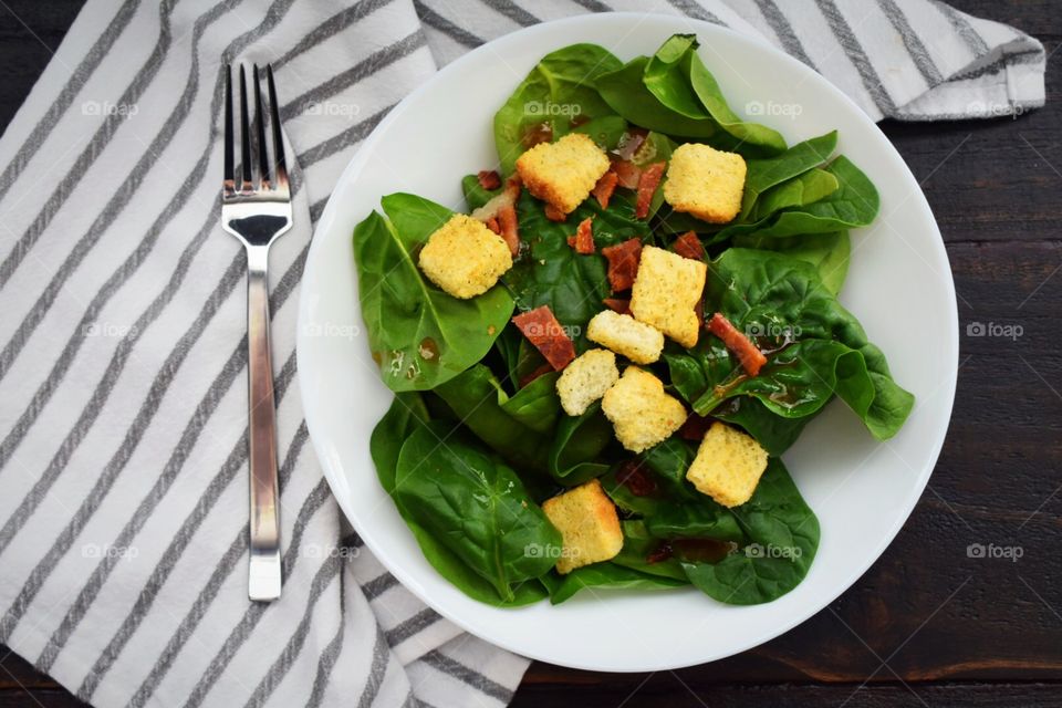 Spinach salad topped with bacon, croutons, and dressing