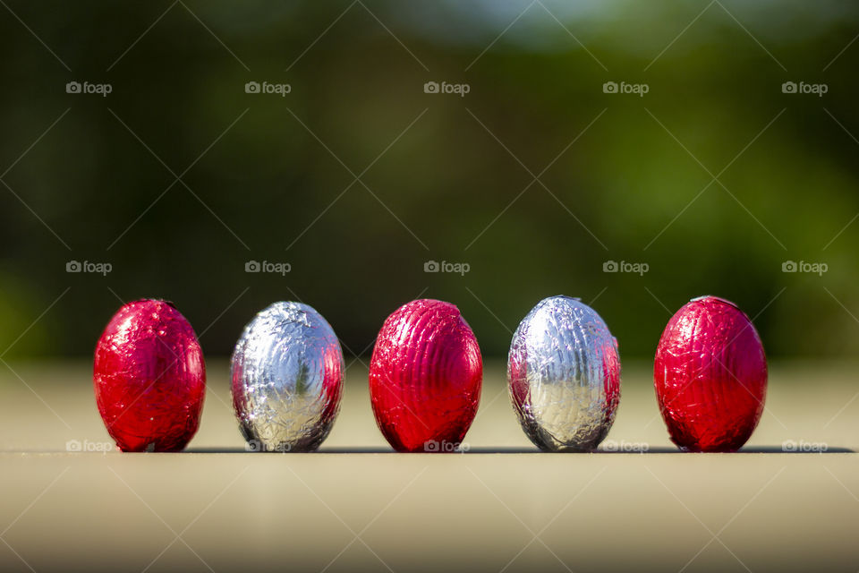 a macro portrait of five chocolate eggs wrapped in red and silver tin foil in a row on a wooden table.