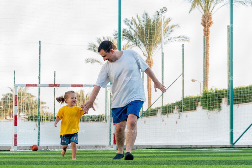 Full body positive man with daughter running together on sports field to camera holding hands