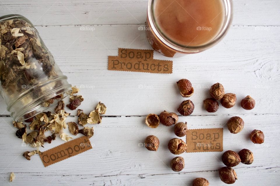 Closeup of soap nuts or soap berries, liquid soap for DIY soap products and used soap nuts/berries for compost on white wooden surface in natural light