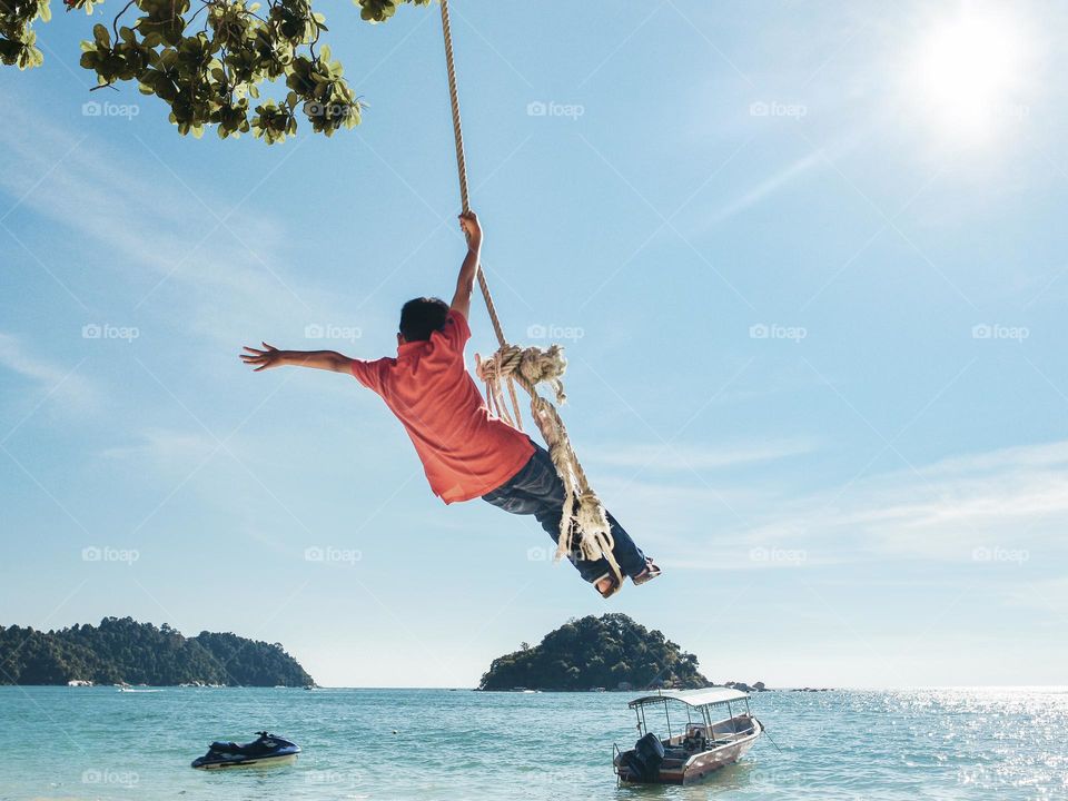 A Boy taking the rope swing alongside sunny beach