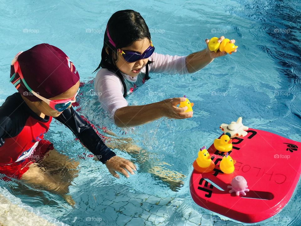 Kids are playing with ducks and toys at swimming pool in summer time 