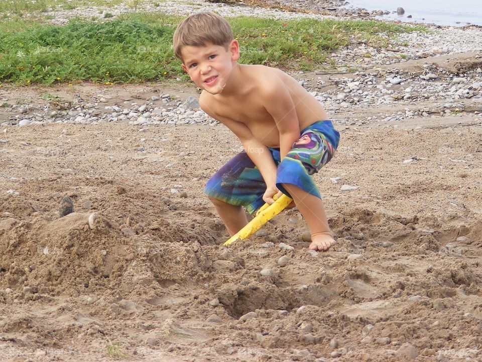 Boy wearing swimming trunks & digging in the sand