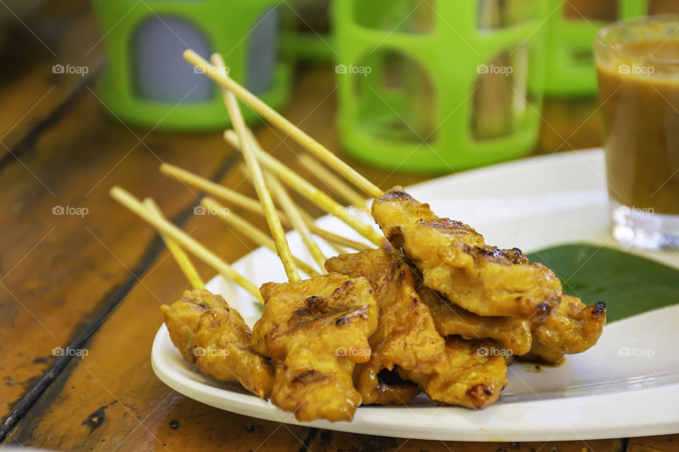 Pork Satay with coconut milk  with  sauce in white plastic plate on wooden table.